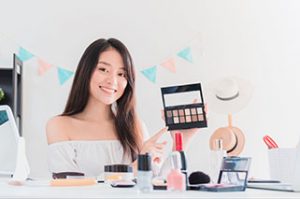 Beautiful asian woman blogger is showing how to make up and use cosmetics. In front of the camera to recording vlog video live streaming at home.Business online influencer on social media concept.